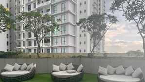 Una terraza en la azotea con tres sofás redondos de mimbre y cojines, rodeada de césped artificial verde.