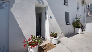 Un edificio blanco con una puerta, plantas en macetas y un felpudo.