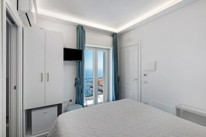 Ein Schlafzimmer mit Bett, Kleiderschrank, Fernseher und einem Balkon mit blauen Vorhängen.