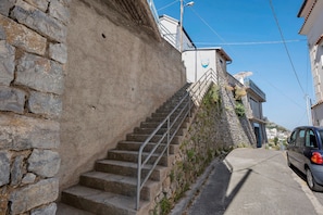 A stone staircase leading to a building with a balcony, a parked car, and a clear sky.