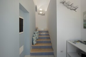 A narrow hallway with a staircase, a wall-mounted light fixture, and a small table with magazines. - Room 'Camera Furore Sea View' with Sea View, Wi-Fi and Air Conditioning (Furore)