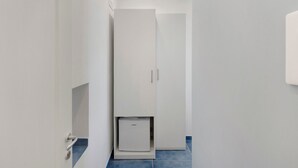 En smal hallgång med en vit dörr längst ner, en liten vit apparat under dörren och ett blått kakelgolv.