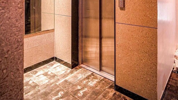 An elevator with a metallic finish, a control panel, and a textured wall. - Roli Residency (Barasat)