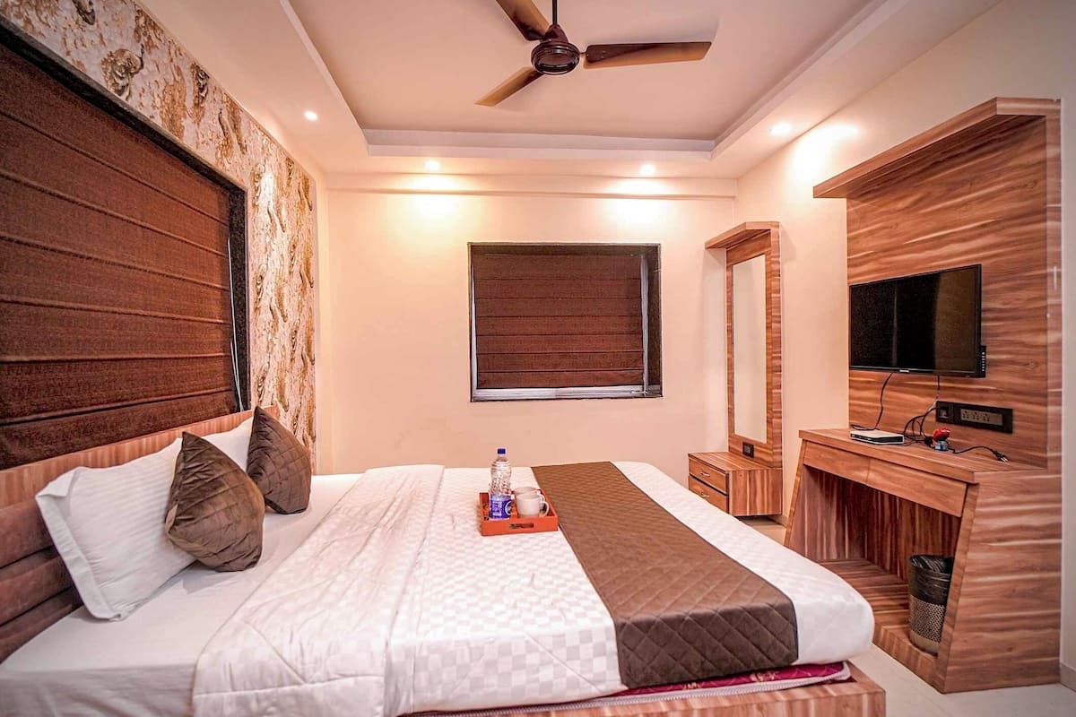 A hotel room with a large bed, a ceiling fan, a TV, and a wooden desk.