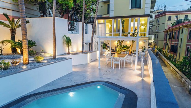 Une piscine dotée d’un espace salon aménagé en contrebas, entourée d’un mur blanc et de palmiers.