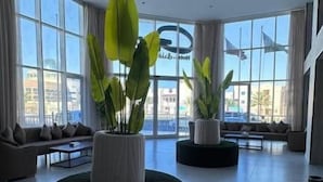 A spacious lobby with large windows, a sofa, and two round black ottomans with potted plants. - Seven Garden Hotel - Airport (Taif)