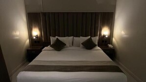 A modern hotel room with a large bed, two bedside tables with lamps, and a wooden headboard. - Seven Garden Hotel - Airport (Taif)