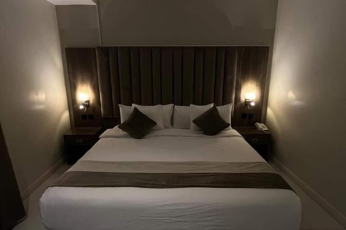 A modern hotel room with a large bed, two bedside tables with lamps, and a wooden headboard.