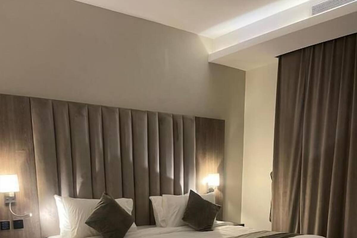 A hotel room with a large bed, two bedside tables, a headboard, and a window with curtains.