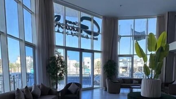 A spacious living area with large windows, a sofa set, a coffee table, and potted plants. - Seven Garden Hotel - Airport (Taif)