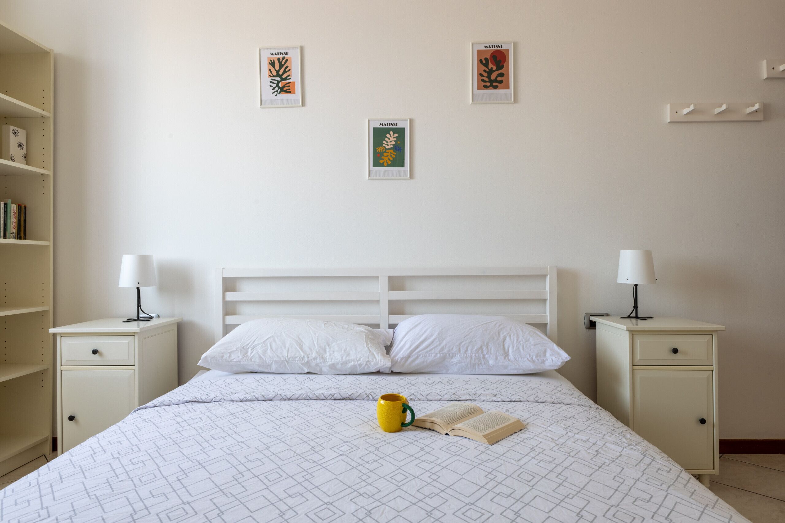 Une chambre à coucher comprenant un lit, deux tables de chevet, une bibliothèque et trois œuvres d’art encadrées accrochées au mur.
