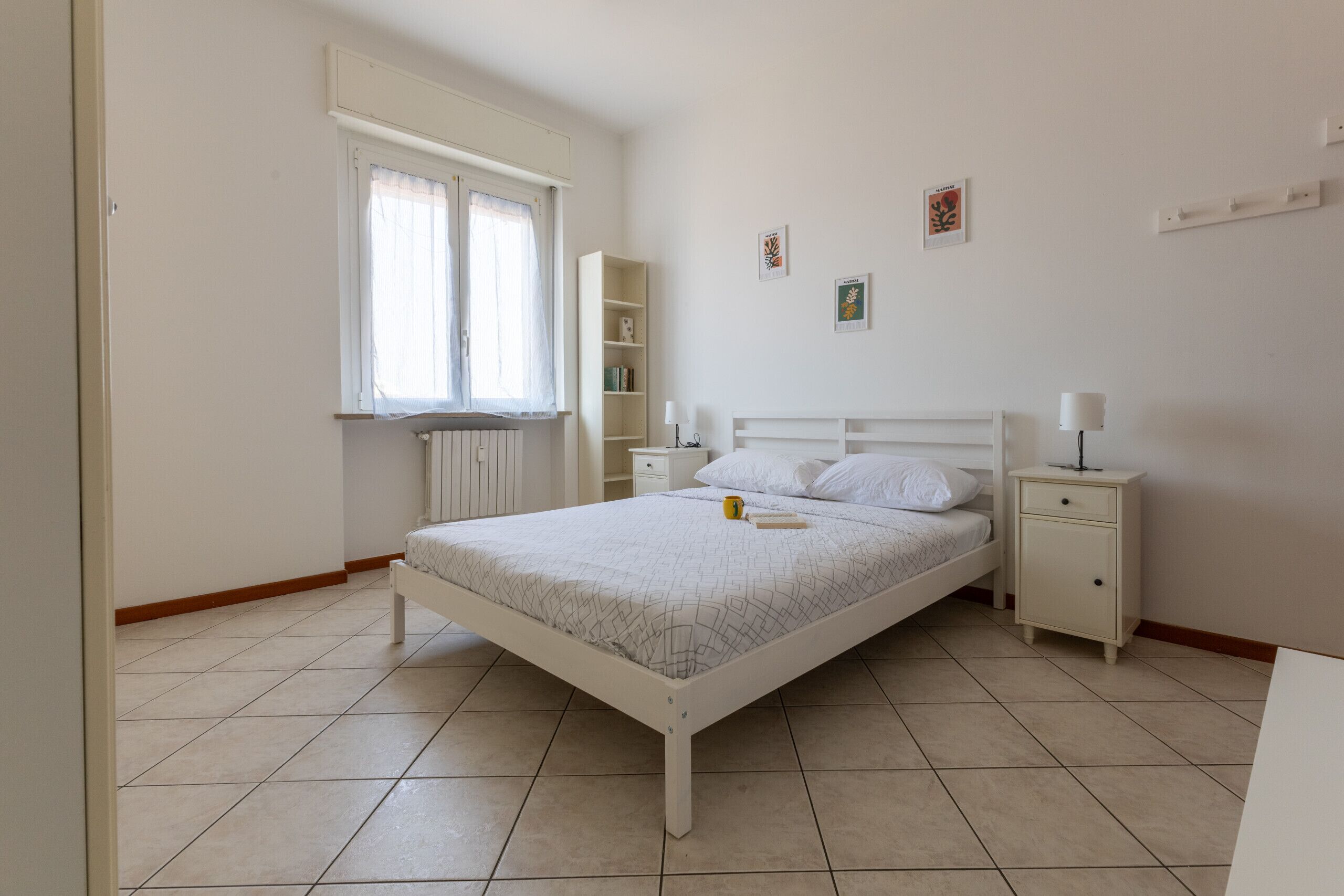 A bedroom with a bed, bedside tables, a window, and a radiator.
