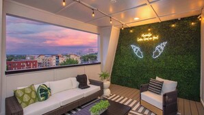 Een modern terras op het dak met uitzicht op de skyline van de stad, een groene wand met neonborden en comfortabele zithoeken.