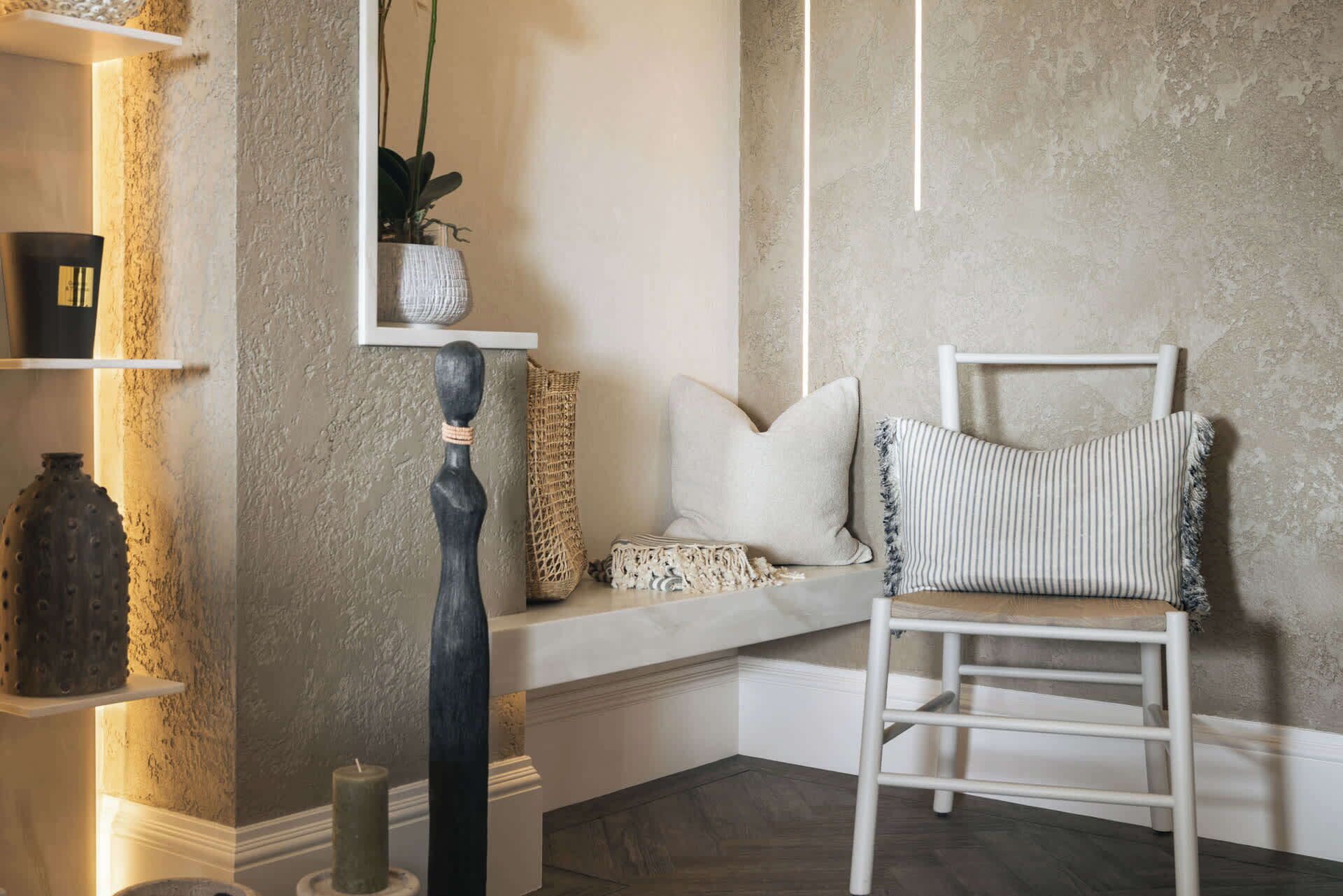 A corner seating area with a white chair, a bench, and decorative pillows.