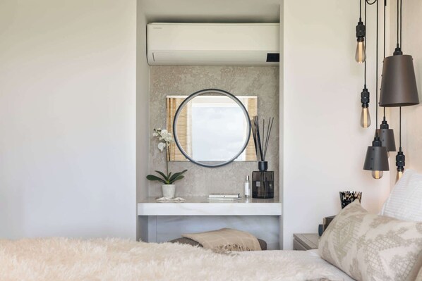 A bedroom with a bed, a bedside table, a mirror, a small shelf with decorative items, and a hanging light fixture.