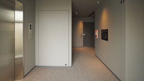 A hallway with a closed elevator door, a wall-mounted emergency phone, and a door with a number plate. - UCHIWA STAY Osaka NAMBA (Osaka)