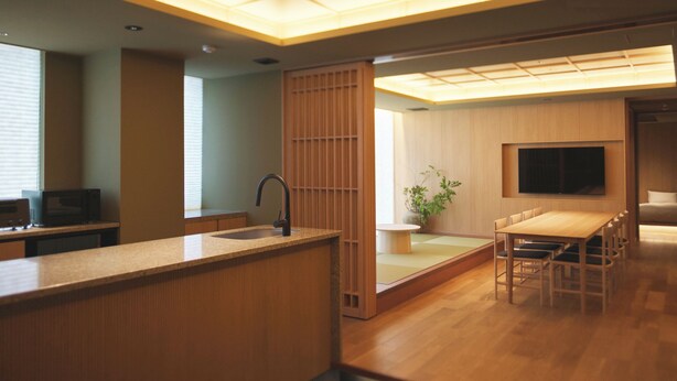 A modern kitchen with a wooden countertop, a sink, and a microwave. There is a dining area with a table and chairs, and a TV mounted on the wall. - UCHIWA STAY Osaka NAMBA (Osaka)