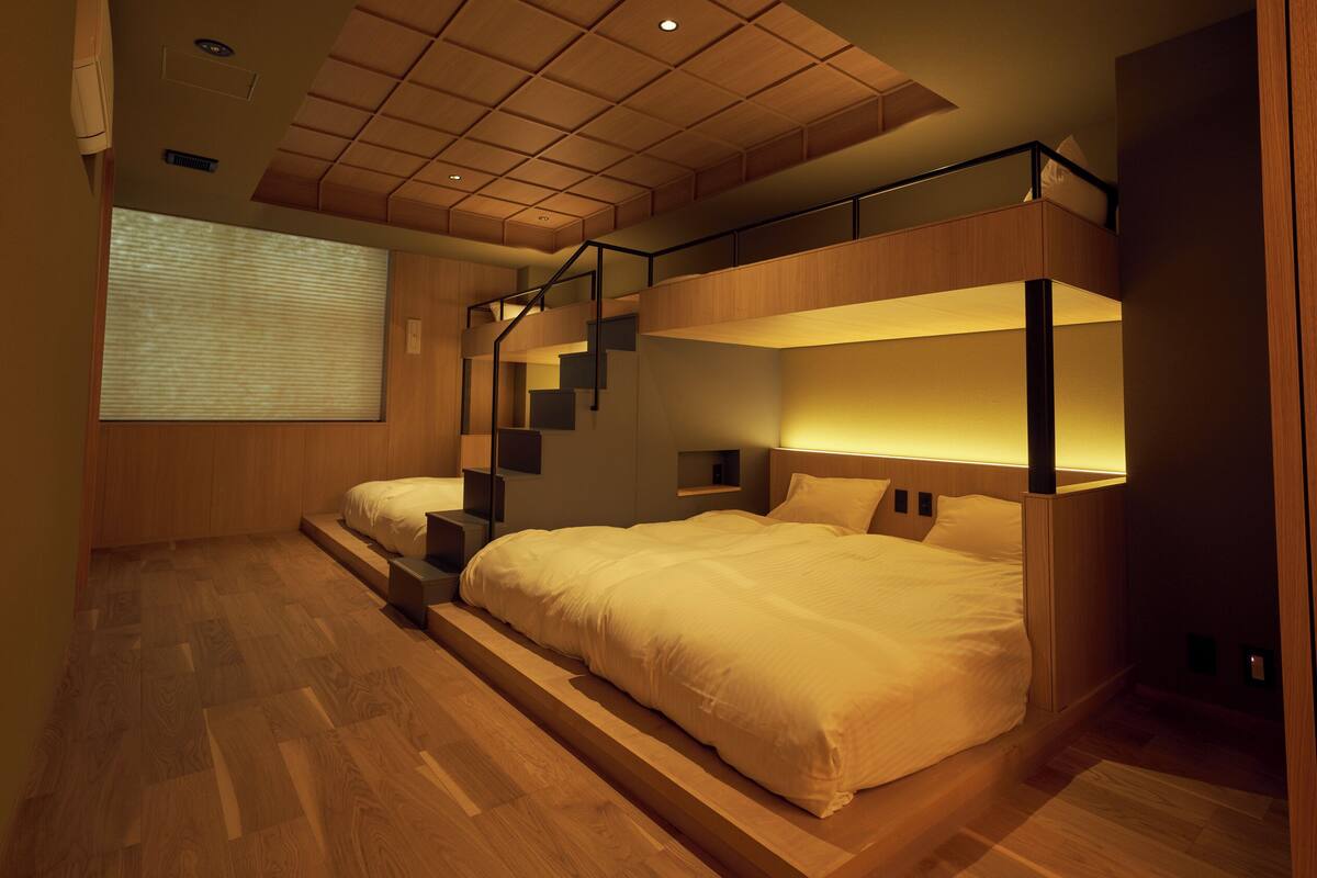 A modern bedroom with a bunk bed, wooden flooring, and a staircase leading to an upper level.