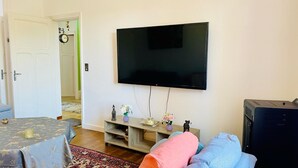 A living room with a flat-screen TV mounted on the wall, a wooden entertainment unit with decorative items, a sofa, and a coffee table. - VILLA COSY (fumel)