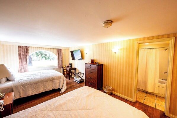 A hotel room with two beds, a desk, a TV, and a shower.