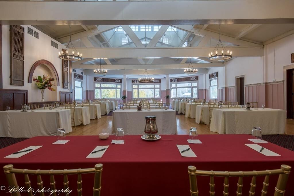 A banquet hall with multiple round tables, white tablecloths, and red table runners.