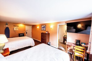 Habitación de hotel con dos camas, un escritorio, una silla, un televisor y una puerta que da a un baño.