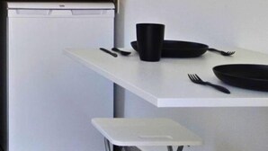 Una cocina pequeña con una encimera blanca, un tazón negro y un taburete blanco.
