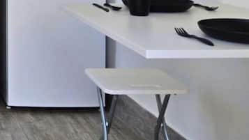 Un espace cuisine compact doté d’un plan de travail blanc, d’un saladier noir et d’un tabouret blanc.
