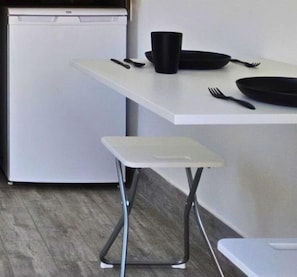 Un angolo cottura compatto con un piano di lavoro bianco, una ciotola nera e uno sgabello bianco.