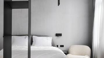 A modern hotel room with a bed, a desk with a magazine and glasses, a chair, and a unique black and white decor.
