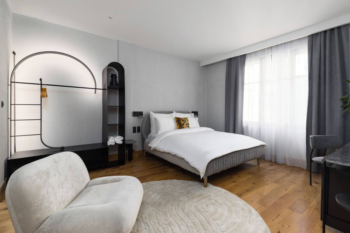 A modern bedroom with a bed, a chair, a desk, and a mirror.