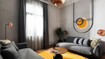 Een moderne woonkamer met een grijze bank, een ronde salontafel en een groot raam met dunne gordijnen.