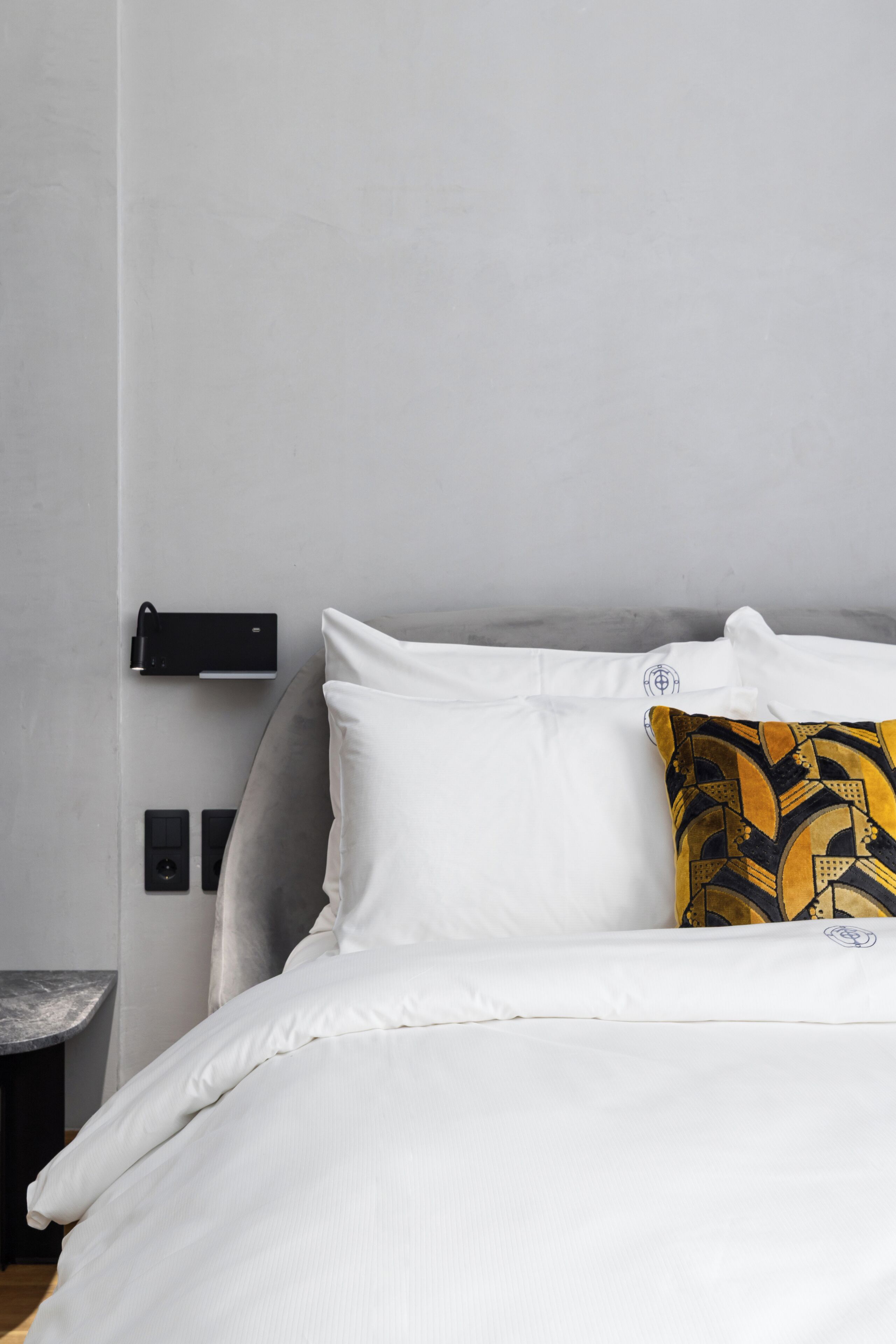 Een net opgemaakt bed met witte beddengoed en één decoratief kussen.