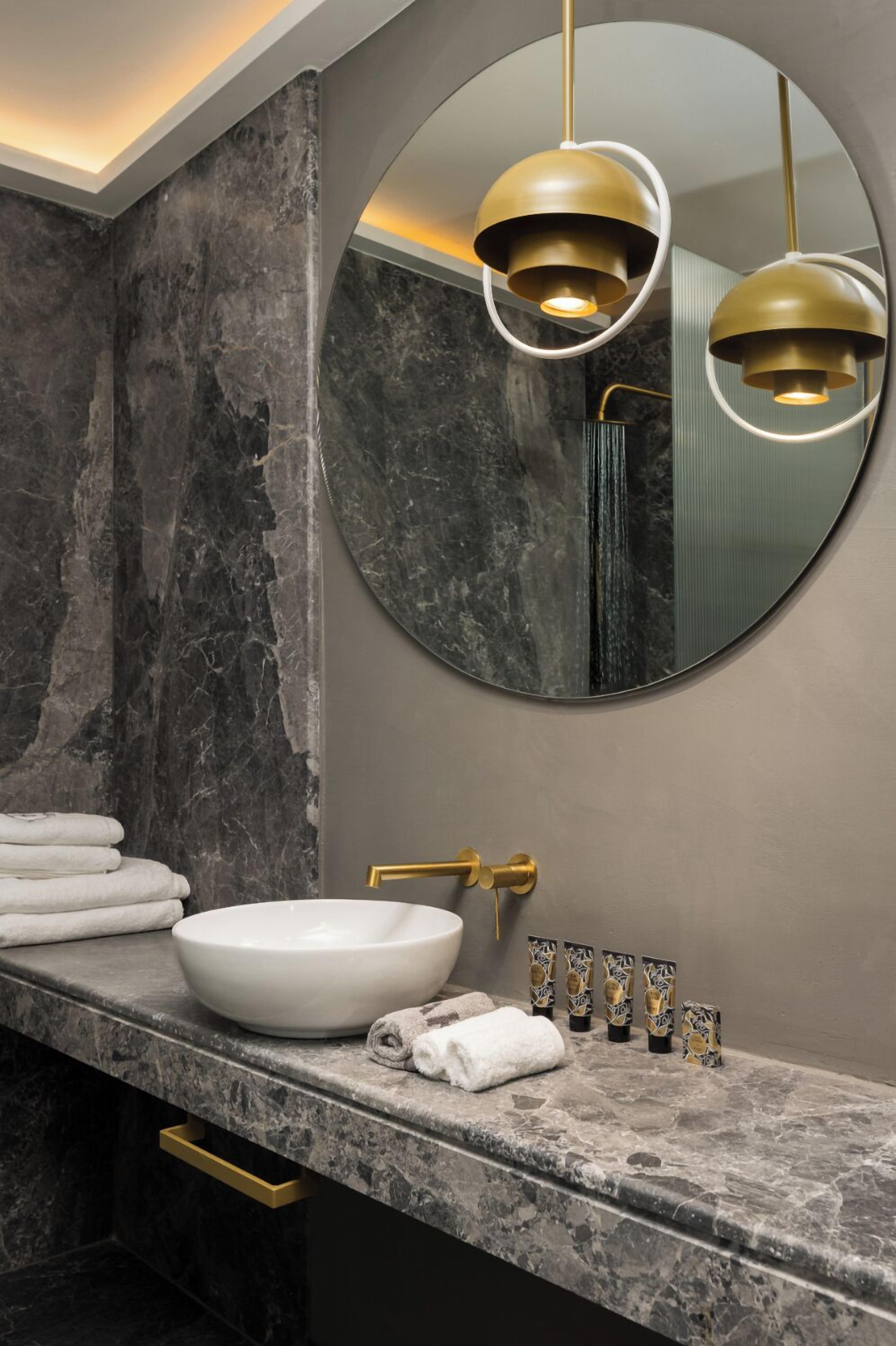 A modern bathroom with a marble sink, gold fixtures, and a round mirror.