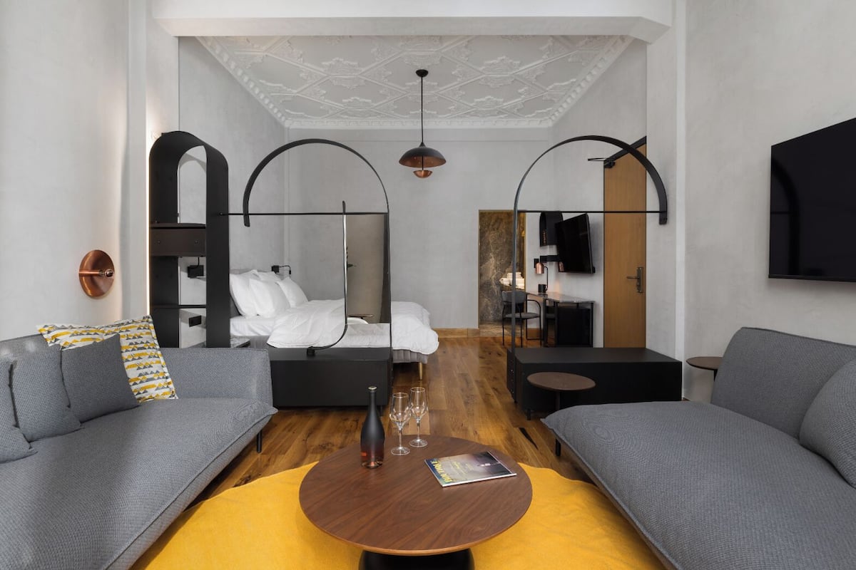 A modern hotel room with a bed, two sofas, a coffee table, and a TV mounted on the wall.