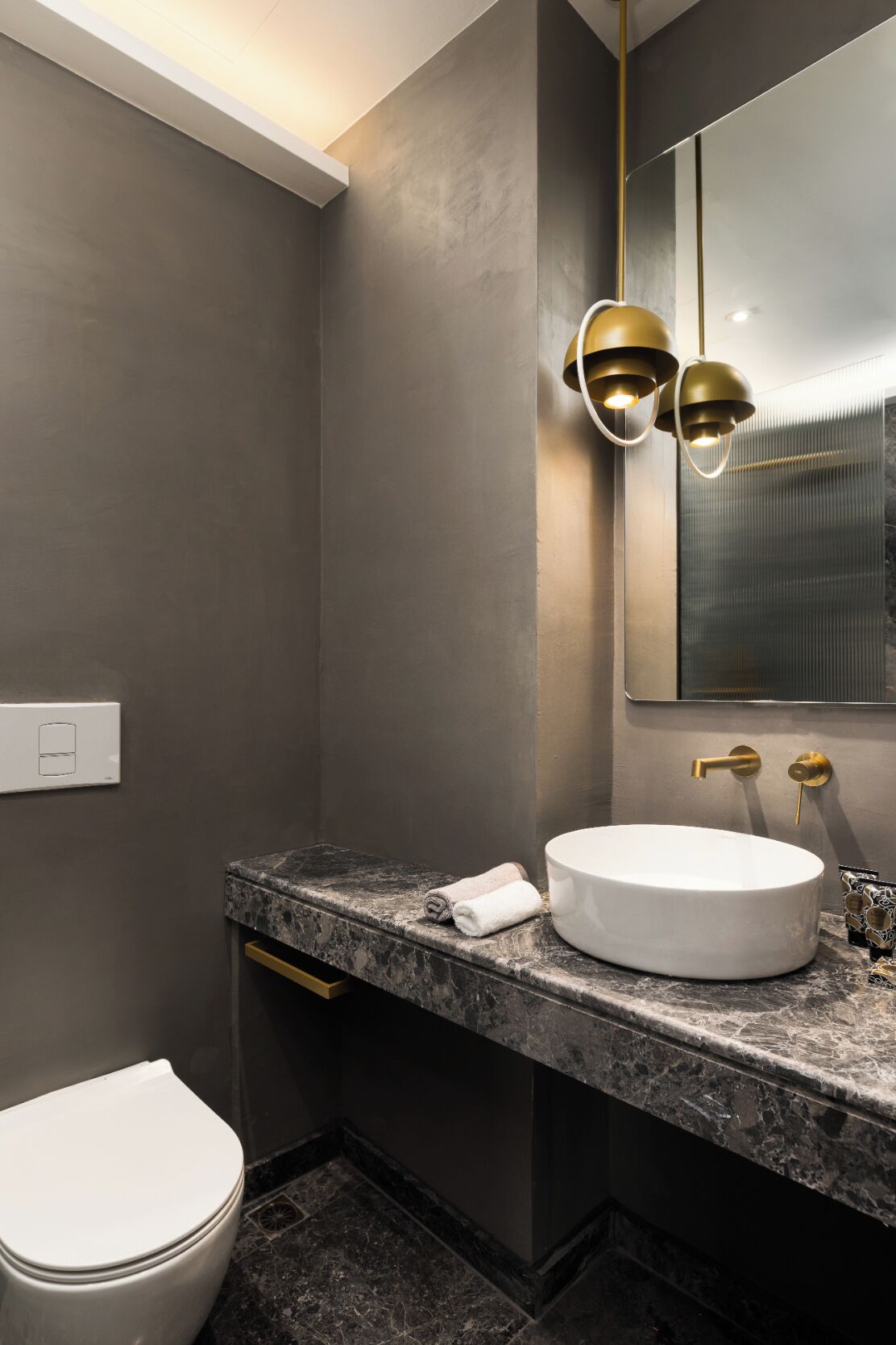 A modern bathroom with a marble countertop, a round sink, and a toilet.