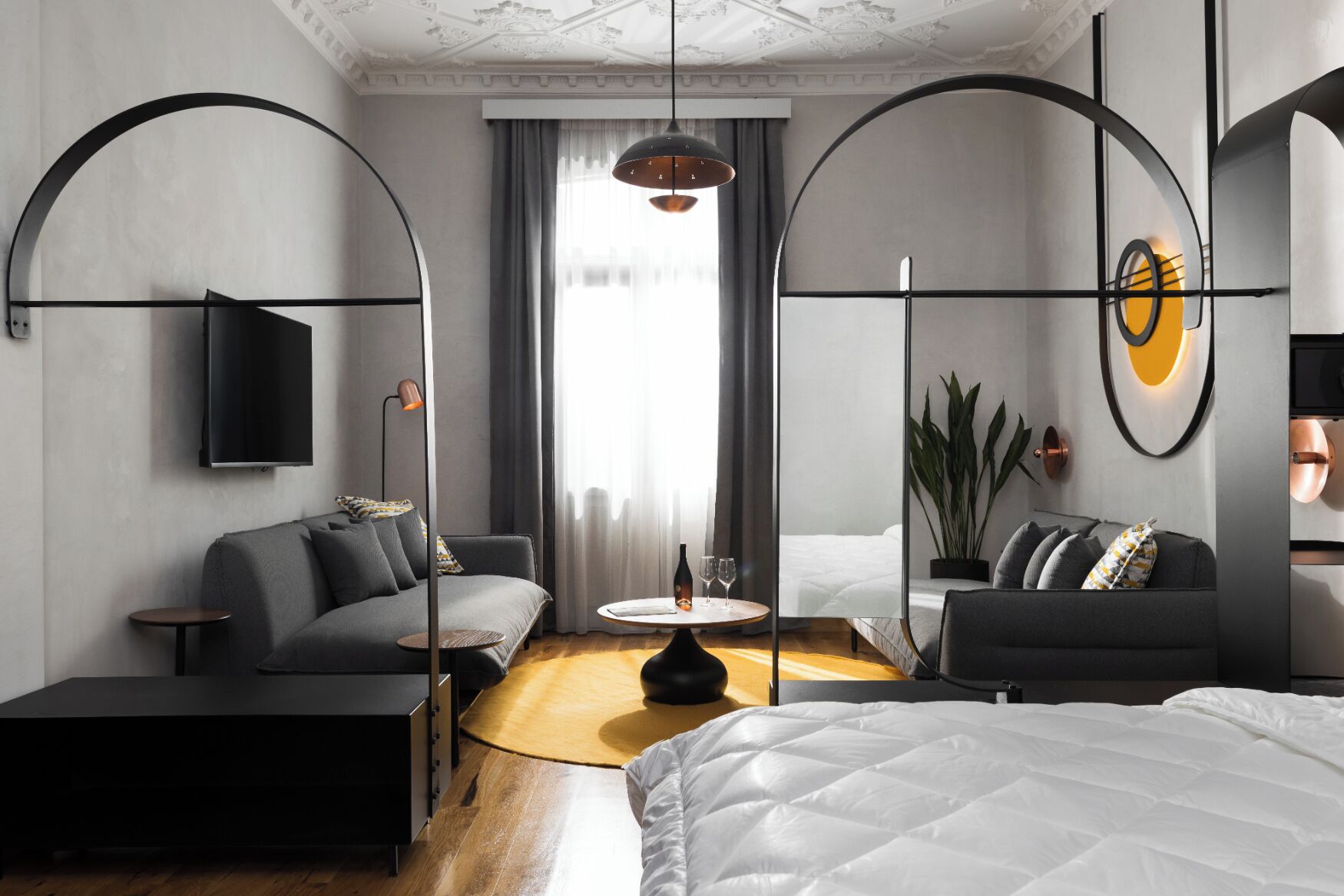 A modern hotel room with a sofa, a bed, a small table, and a TV mounted on the wall.