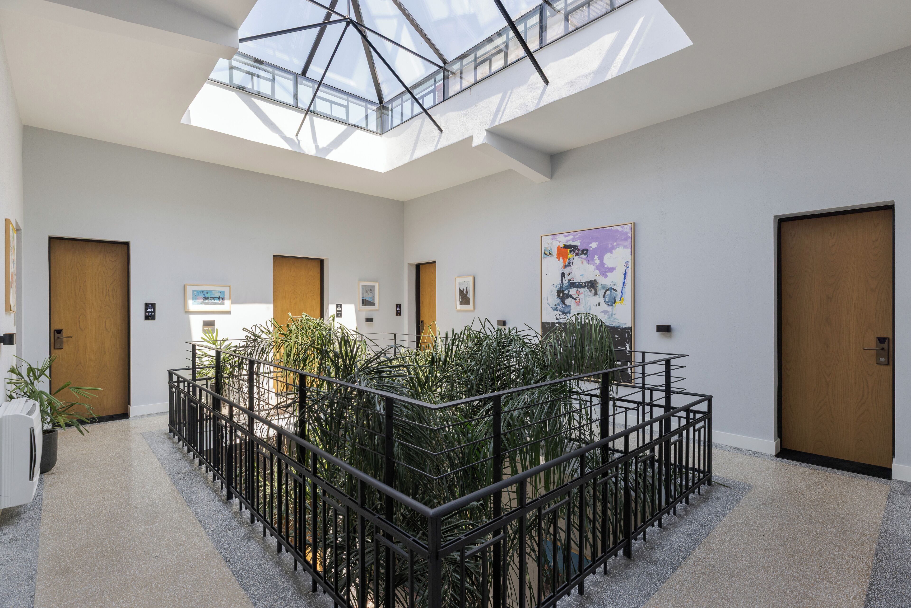 A modern interior with a central plant area, skylight, and wooden doors.
