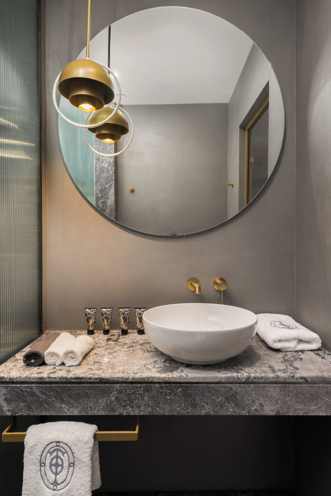 Een moderne badkamer met een ronde spiegel, een witte wastafel en gouden details.