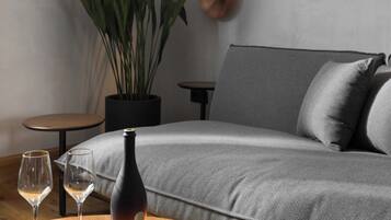 Un salon moderne avec un canapé gris, une table basse ronde sur laquelle se trouvent une bouteille et des verres, une plante en pot et une lampe fixée au mur.