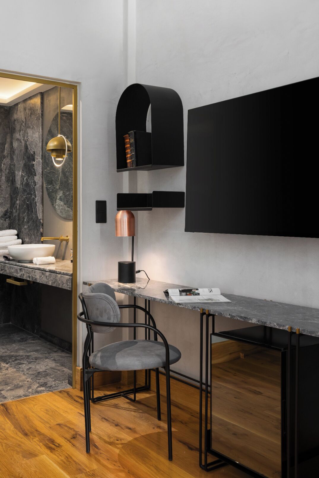 Un baño moderno con tocador de mármol, una lámpara colgante dorada y un lavabo negro.