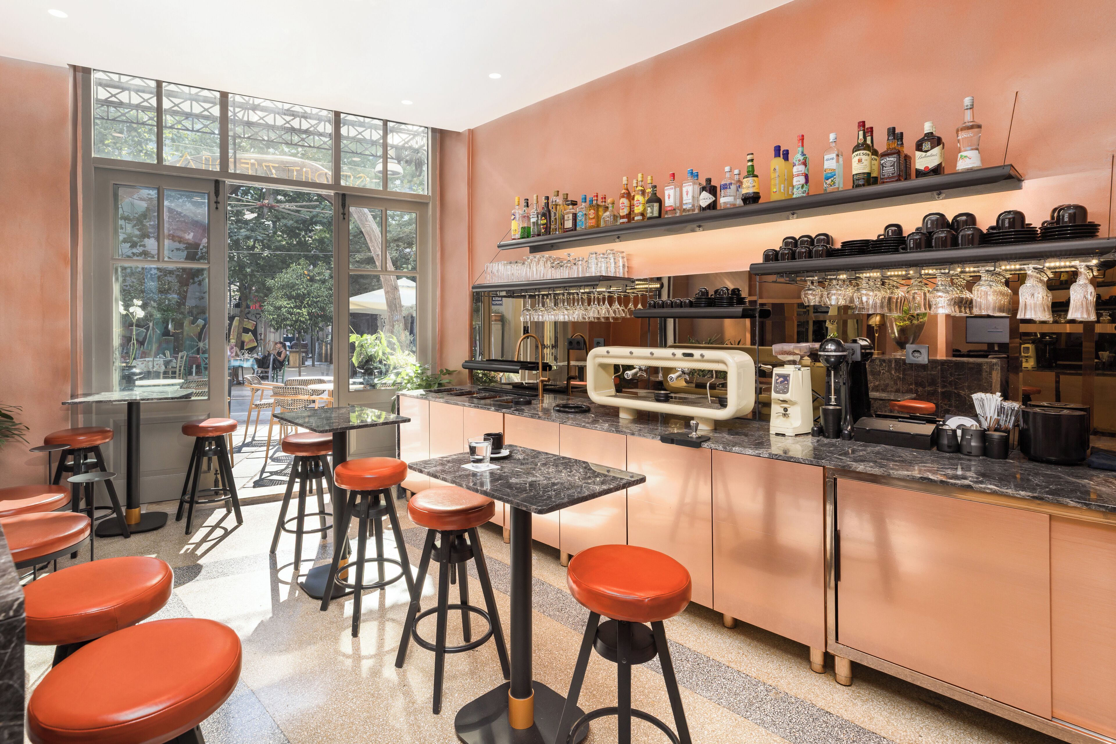 Een bar met krukken, een aanrecht met flessen en glazen, en een groot raam.