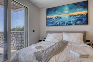 A modern bedroom with a large bed, a view of the outdoors through a glass door, and a painting on the wall.
