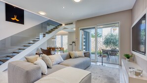 A modern living room with a grey sectional sofa, a glass staircase, and a large TV on the wall.