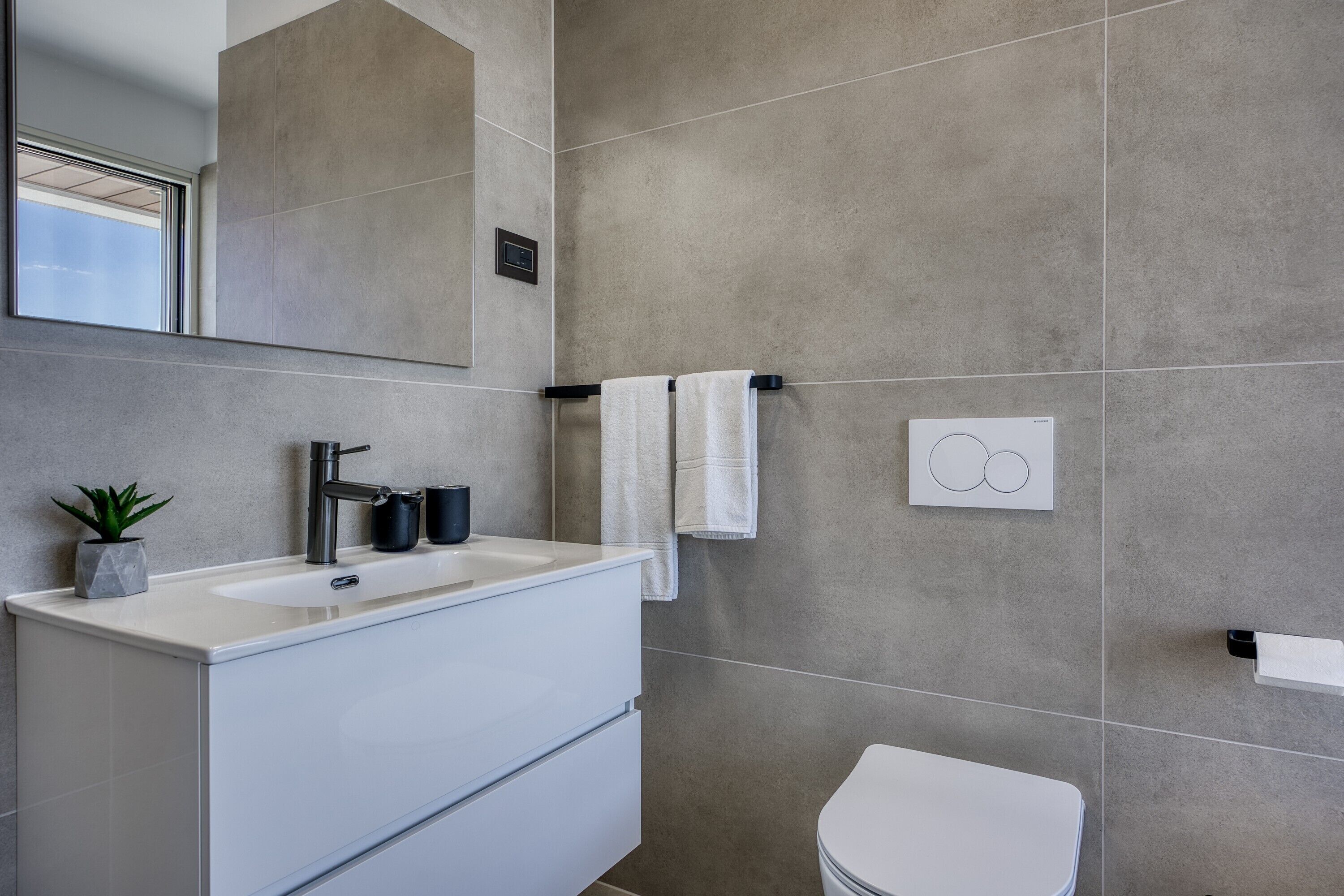 A modern bathroom with a white sink, a mirror, a towel rack, and a toilet.