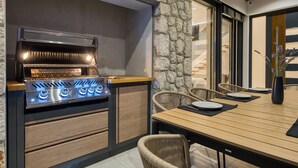 An outdoor kitchen with a stone wall, a wooden table set for dining, and wicker chairs.