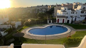 Ein Wohngebiet mit einem runden Swimmingpool, umgeben von einem weißen Zaun, vor dem Hintergrund weißer Gebäude und eines klaren Himmels.