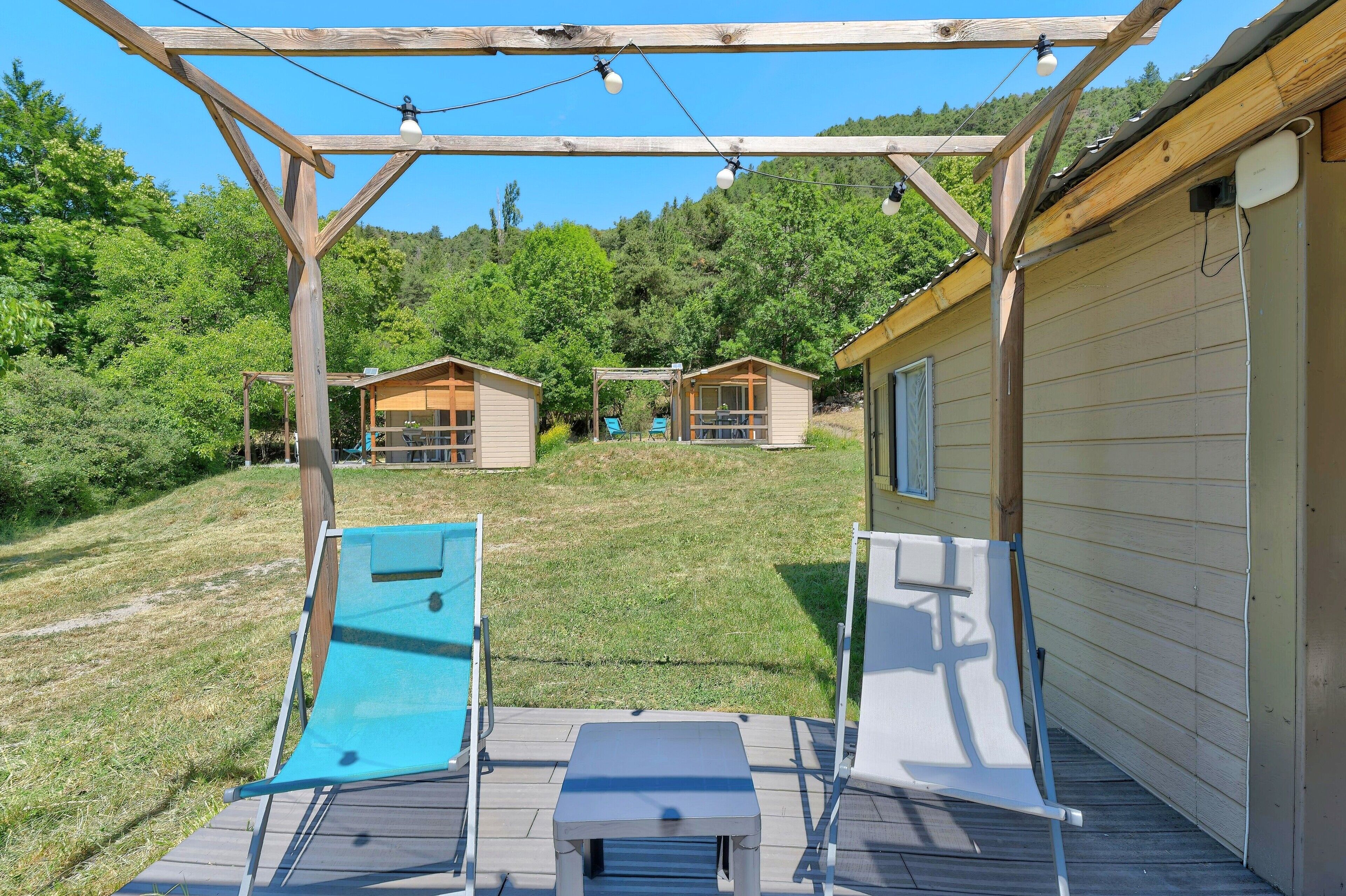 Une terrasse en bois avec une table et des chaises, un toboggan et deux cabanes en arrière-plan.