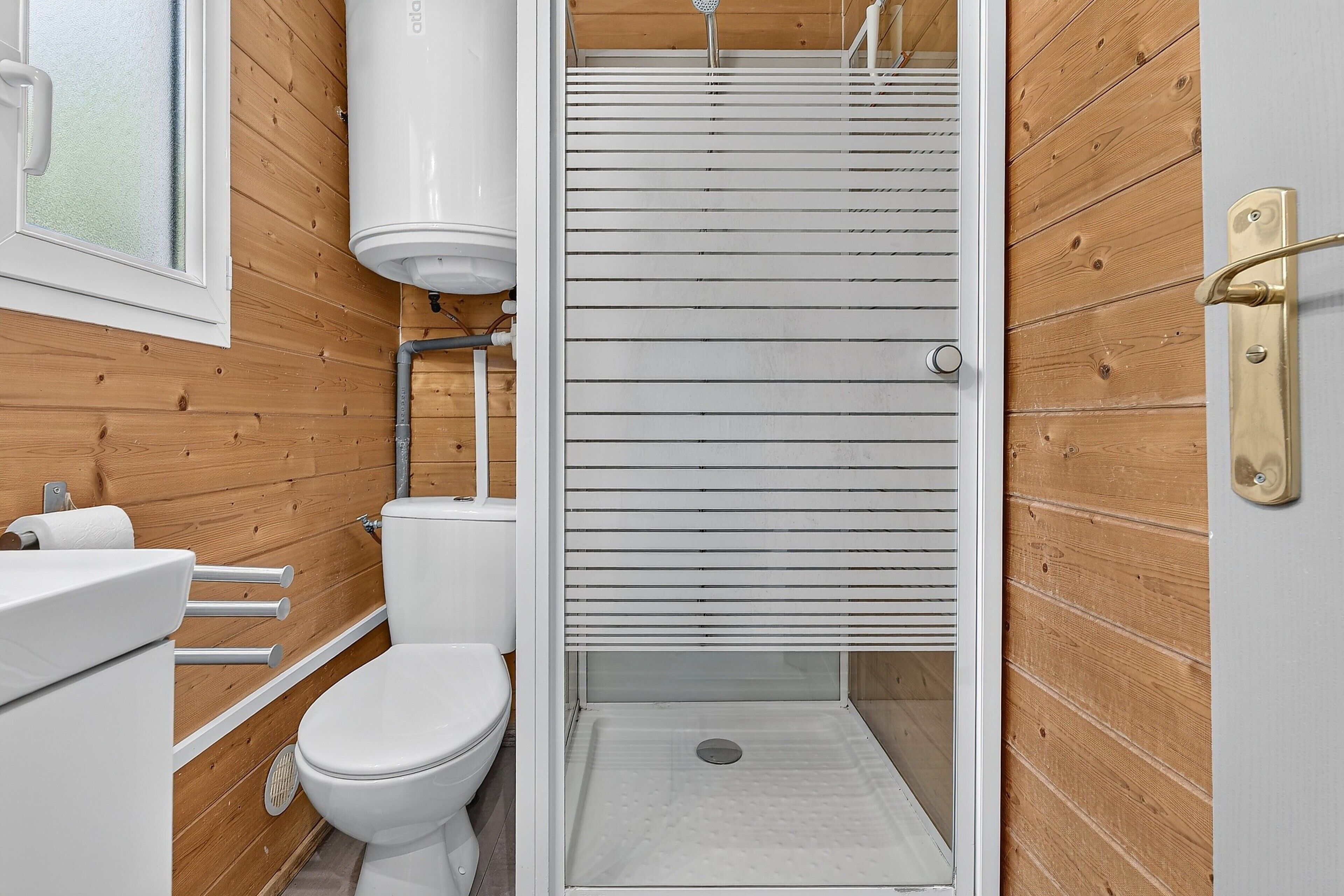 A bathroom with a wooden wall, a white toilet, a shower with horizontal blinds, and a white sink.