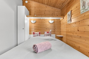 A room with wooden walls, a bed with a pink towel, a white wardrobe, and a small white table. - Cottage "Morgon" with Mountain View, Wi-Fi and Air Conditioning (Crots)